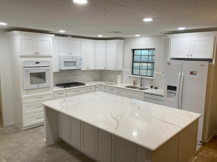 Remodeled kitchen in North Bryan with a Carrara-look quartz island, white shaker cabinets to the ceiling, and quartz backsplash